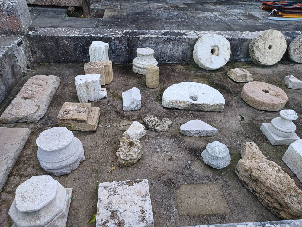 Various ancient stone artifacts, including columns and millstones, are displayed on the ground at Castelo de São Jorge.