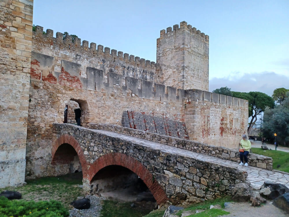 The entrance to Castelo de São Jorge, featuring a stone bridge with red brick arches leading to the castle.