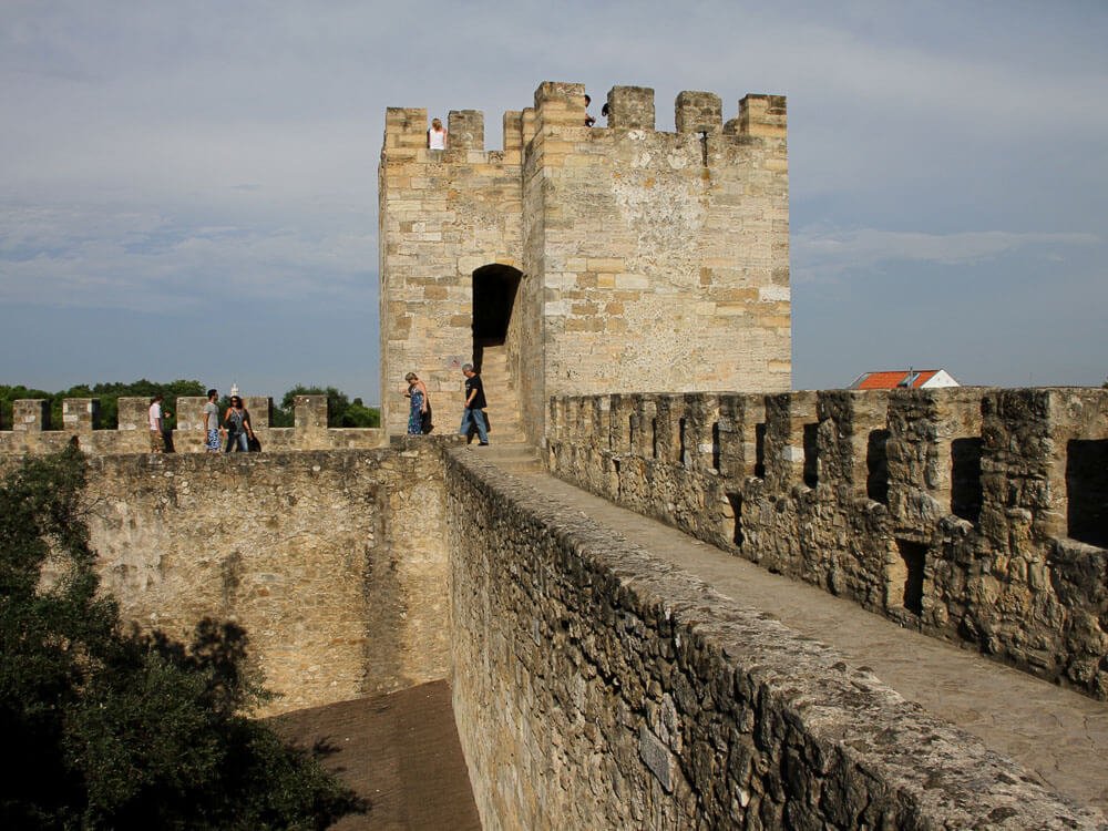 Stone battlements where several people are seen walking along the fortified walls.