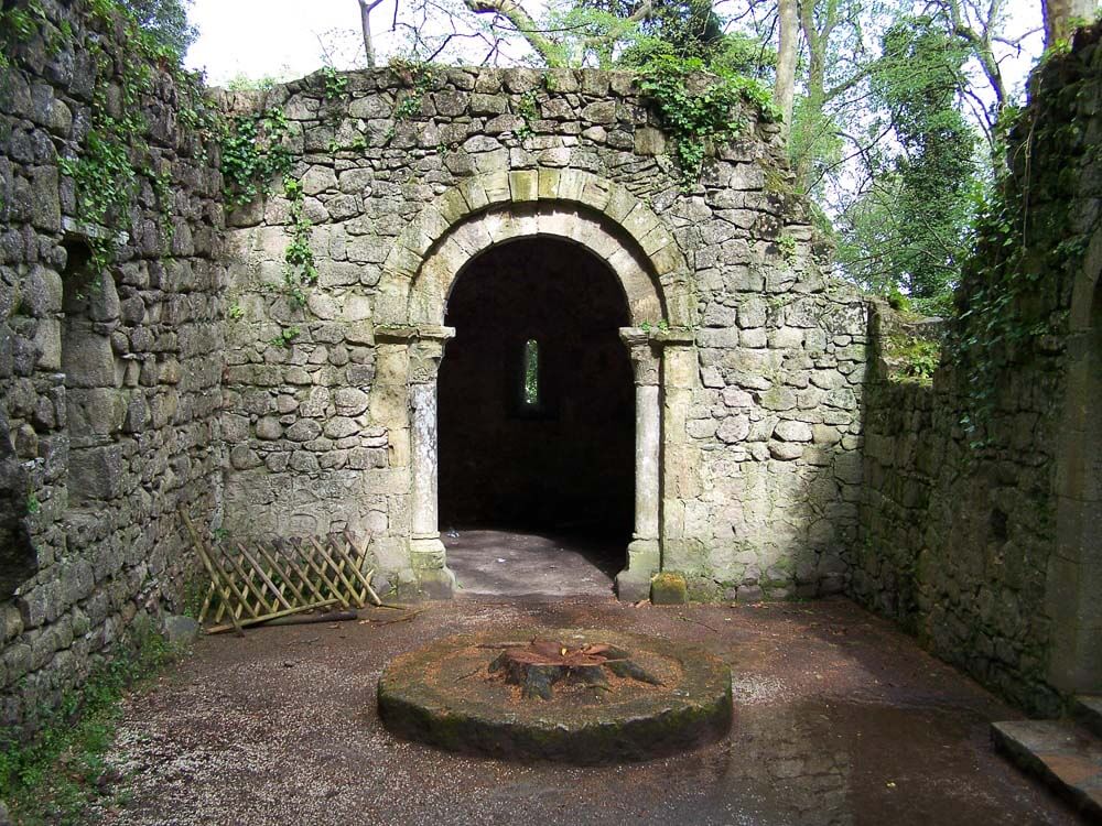 Ruins of a stone structure with an arched entrance, surrounded by walls covered in greenery.