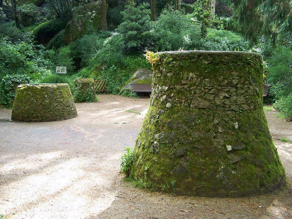 Two large stone bases covered in moss, situated in a forested area.