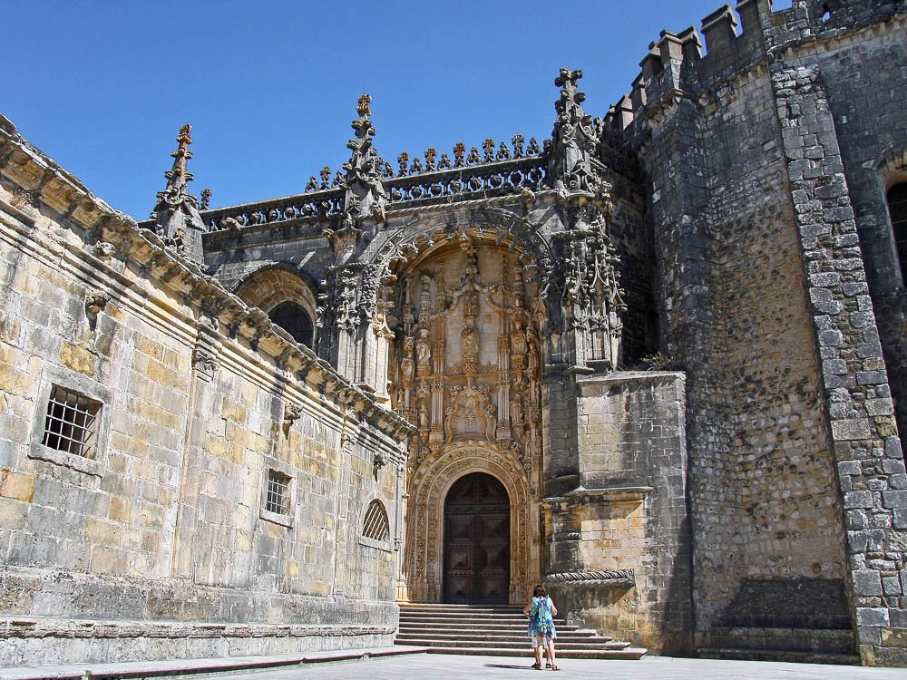 The richly decorated entrance to the Convent of Christ, with intricate carvings and a visitor standing in front of the doorway.