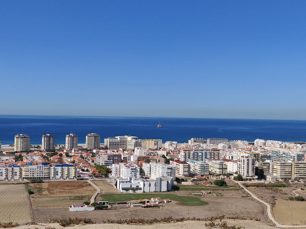 Panoramic view of the coastal city of Costa da Caparica with modern buildings, looking out over the ocean on a clear day.