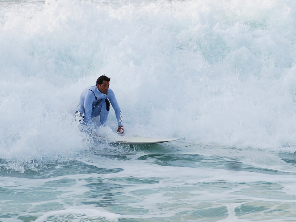 A surfer riding a wave in the ocean of Costa da Caparica, surrounded by white foam from the crashing waves.