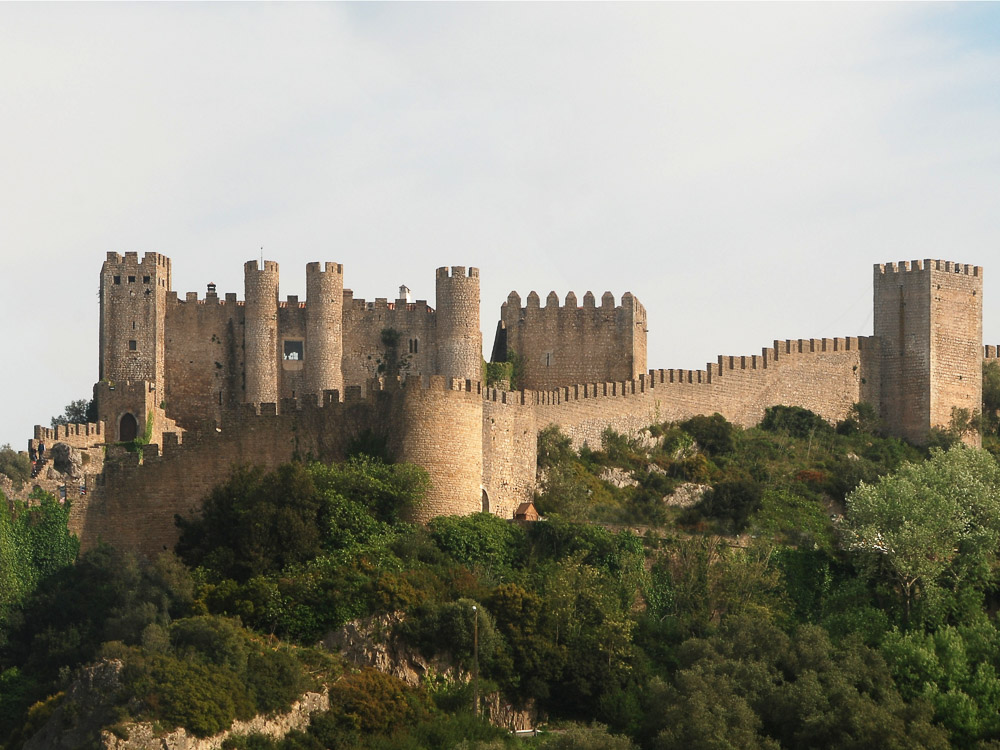 The medieval walls and towers of the well-preserved Óbidos Castle, surrounded by lush greenery.