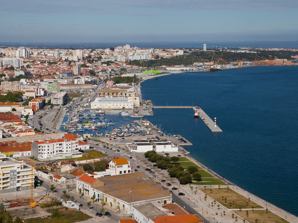 An aerial view of a coastal city with a marina, showing boats, docks, and buildings along the shoreline.