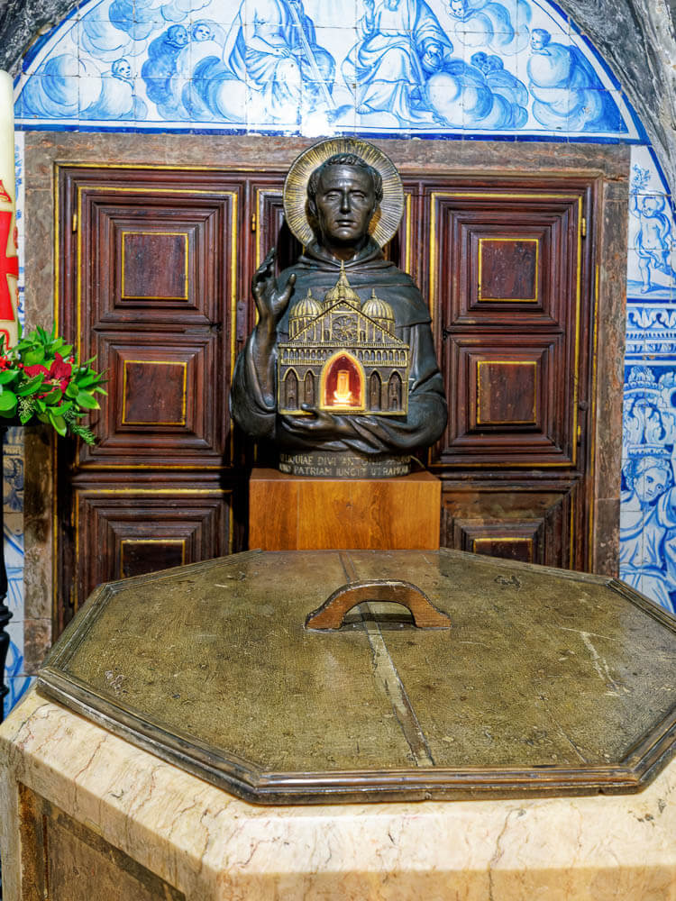 The St. Anthony baptismal font, located inside a chapel within the Lisbon Cathedral, with intricate blue and white tiles on the wall behind it.