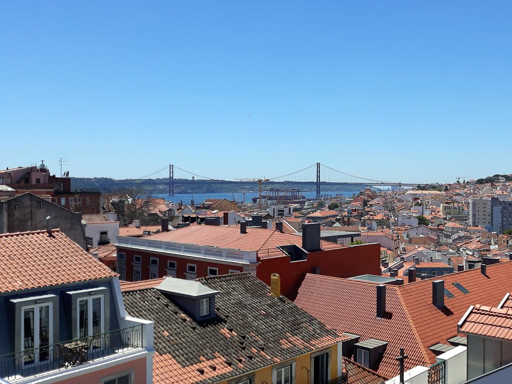 A view of Lisbon’s rooftops with the 25 de Abril Bridge in the distance on a clear day.