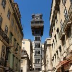 The Santa Justa Lift seen from a street between two rows of buildings, rising high above the rooftops.