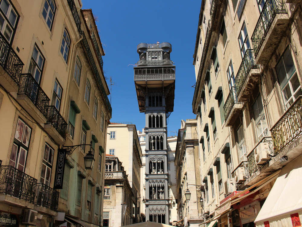 The Santa Justa Lift seen from a street between two rows of buildings, rising high above the rooftops.