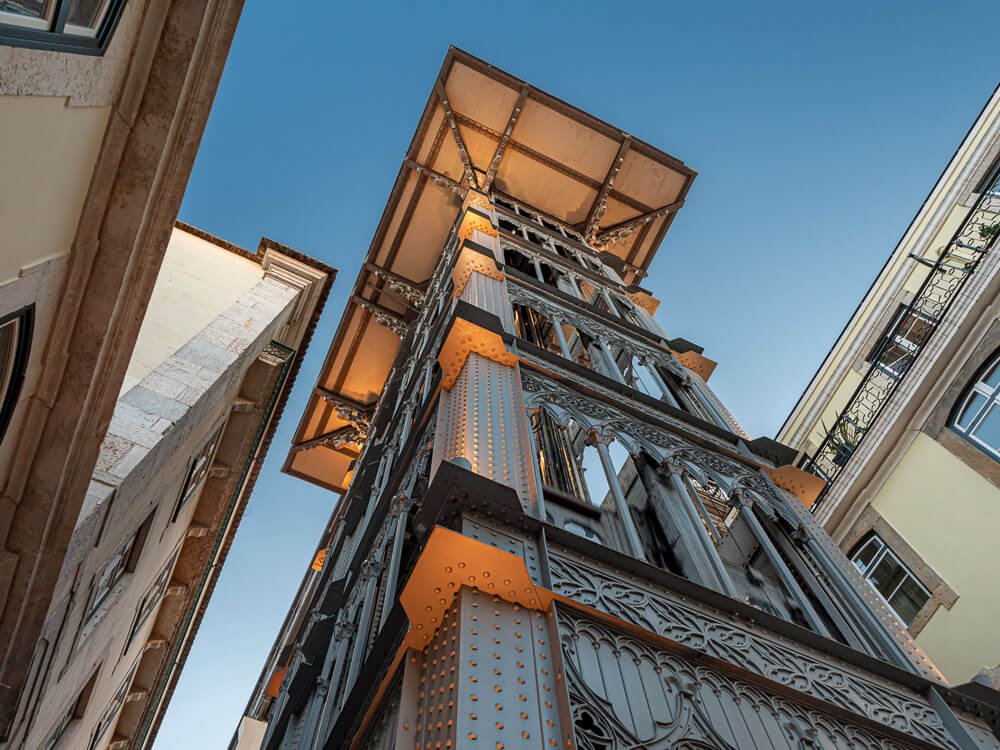 An upward view of the Santa Justa Lift, showcasing its detailed iron structure against a clear blue sky.