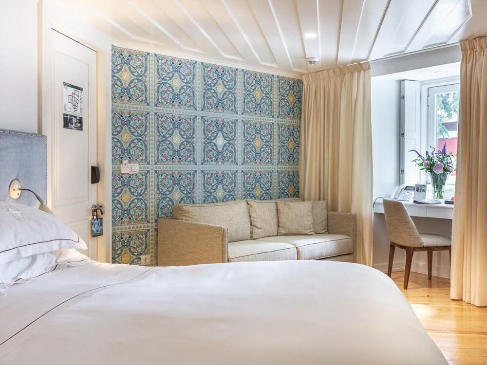 Bright boutique hotel room with a colorful tile accent wall, a beige couch, and a work desk near the window in Lisbon.