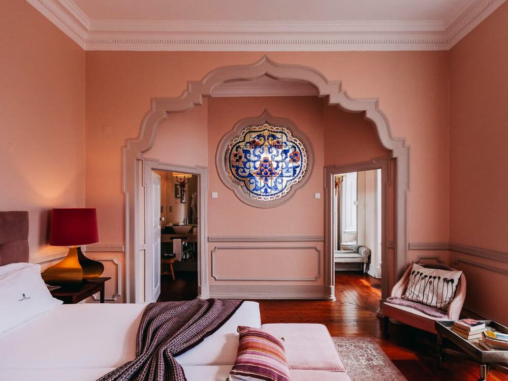 Elegant boutique hotel room with soft peach walls, an archway with intricate detailing, and a decorative wall tile in Lisbon.