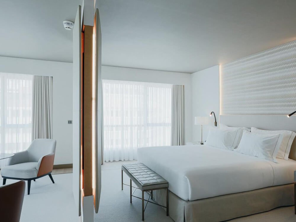 Bright, all-white hotel room with large windows, minimalistic decor, and soft lighting.