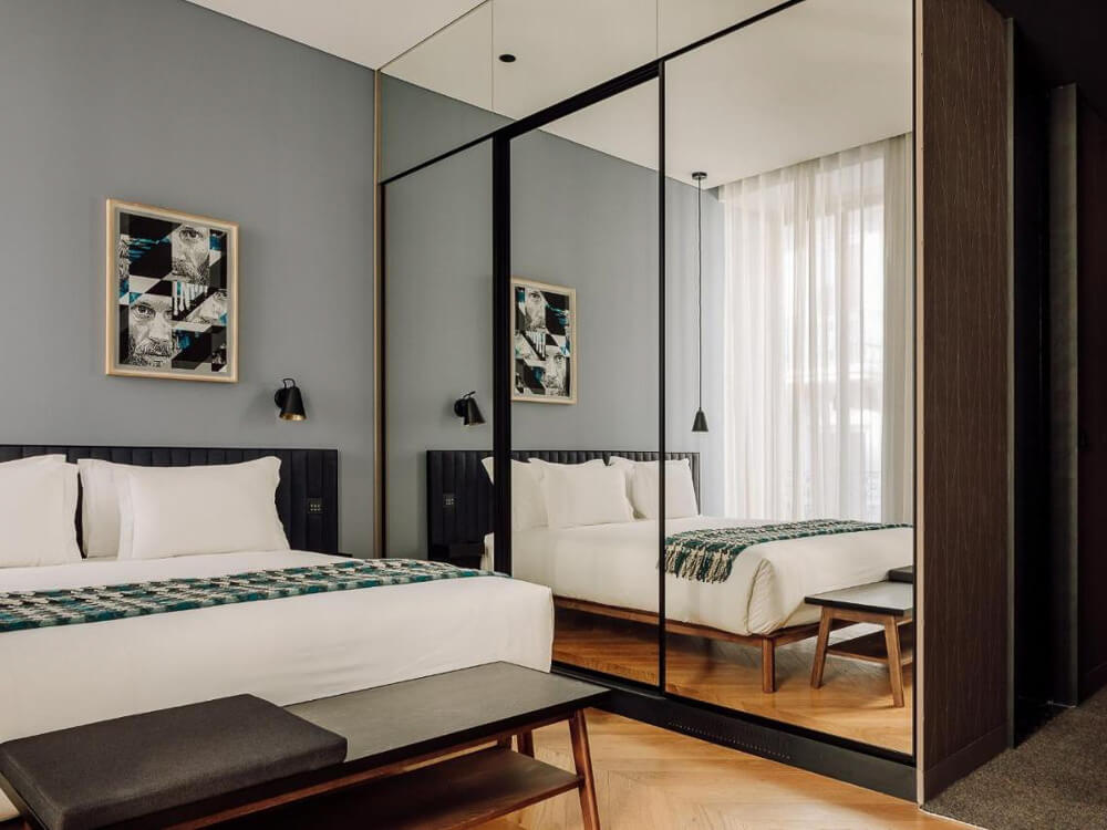 Contemporary hotel room with a minimalist design, mirrored closet doors, and a cozy bed with a patterned throw.