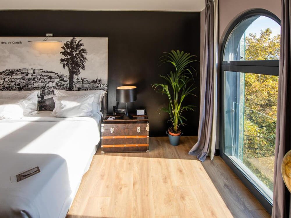 Stylish hotel room with a black accent wall, a large arched window, and a decorative headboard featuring Lisbon scenery.