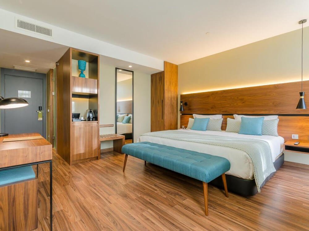 Modern boutique hotel room with sleek wooden furniture, a king-size bed, and a blue bench at the foot of the bed.