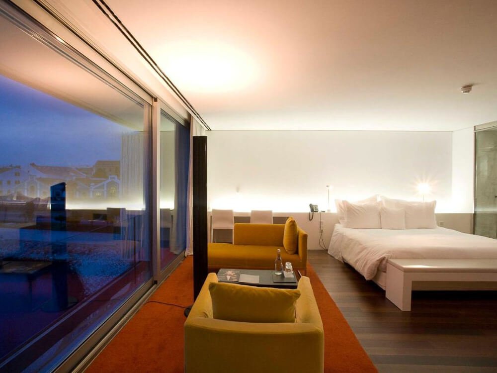 Contemporary hotel room with sleek, minimalist design, featuring a spacious layout, floor-to-ceiling windows, and modern furnishings.