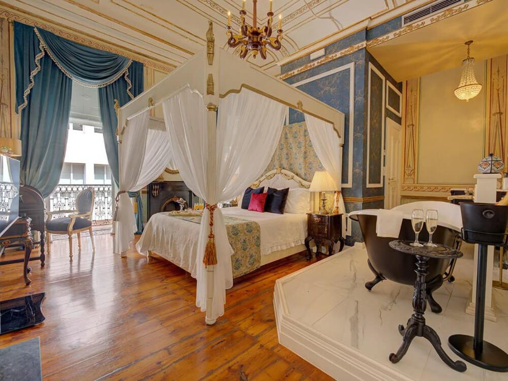 Elegant boutique hotel room with a four-poster bed, royal blue drapes, and a freestanding black bathtub in Lisbon.