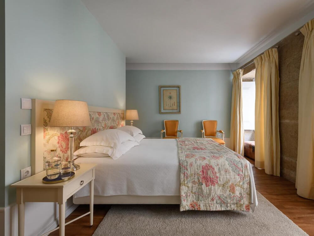 Cozy boutique hotel room with soft pastel colors, floral bedding, and two vintage-style chairs in Lisbon.