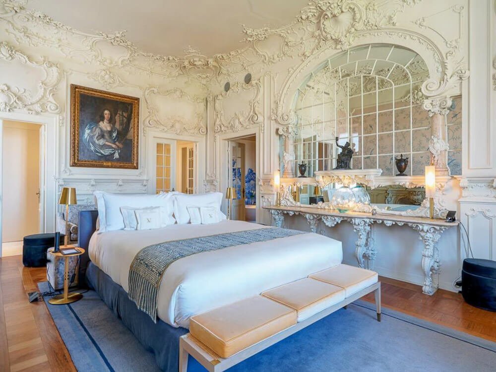 Luxurious boutique hotel room in Lisbon featuring ornate Baroque-style decor, a large bed with white linens, and an elaborate mirror.